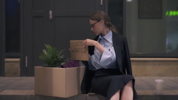 Безнадійна молода жінка, що виконує роботу, розшукує картонний знак, сидячи на вулиці — стокове відео