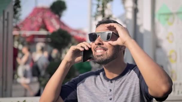 Vrolijke jongeman in zonnebril praten over telefoon buiten — Stockvideo