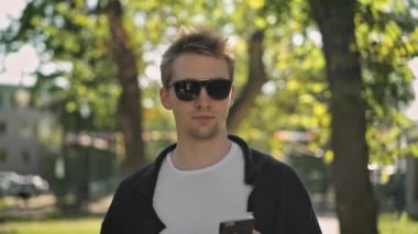 Smartphone cebinden alarak güneş gözlüklü genç adam önden görünümü