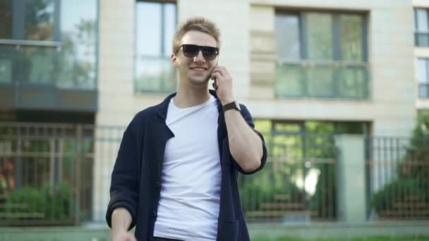 Людина в сонцезахисних окулярах розмовляє по телефону і робить жести перемоги — стокове відео