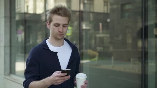 Ernsthafter Mann mit Kaffee beim Spazierengehen und Surfen auf der Straße — Stockvideo