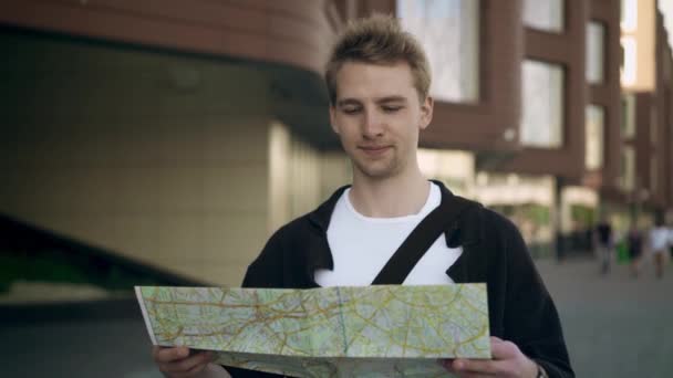 Joven turista con mapa sonriendo y mirando a su alrededor — Vídeo de stock