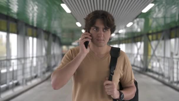 Glimlachend jonge man in beige t shirt praten op smartphone — Stockvideo