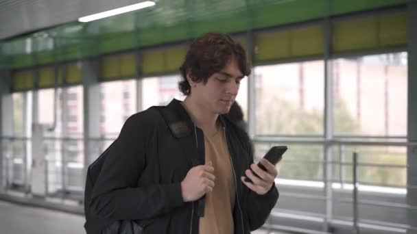 身穿黑色夹克的男子在隧道里散步时采摘智能手机并说话 — 图库视频影像