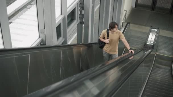 Joven pensativo montando en escaleras mecánicas — Vídeo de stock