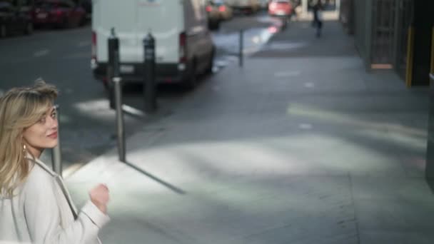 Giovane donna in cappotto bianco che cammina per strada e saluta alla macchina fotografica — Video Stock