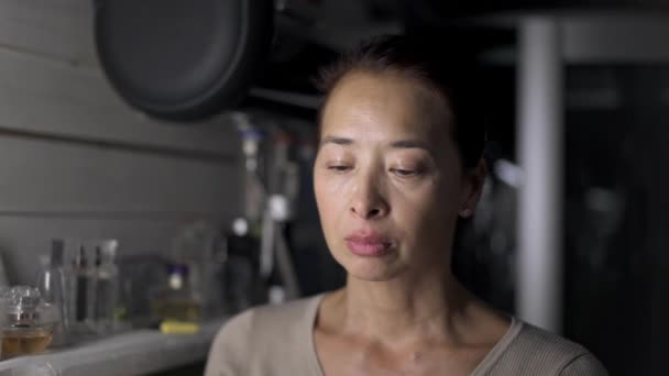 Asiática mujer de mediana edad aplicando crema facial en la cocina — Vídeo de stock