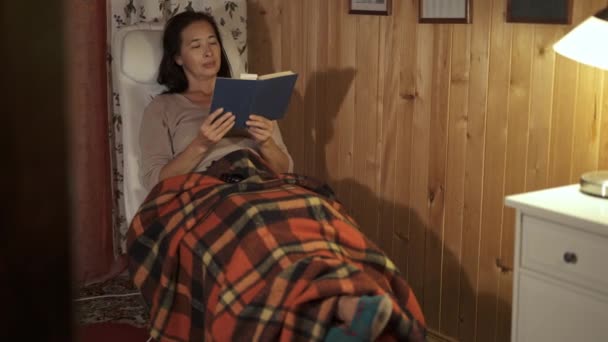 Middelste leeftijd vrouw lezen van een boek in fauteuil met plaid — Stockvideo