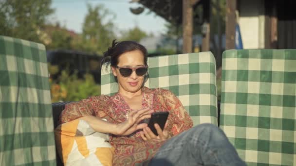 Mediana edad mujer asiática usando smartphone en su patio — Vídeos de Stock