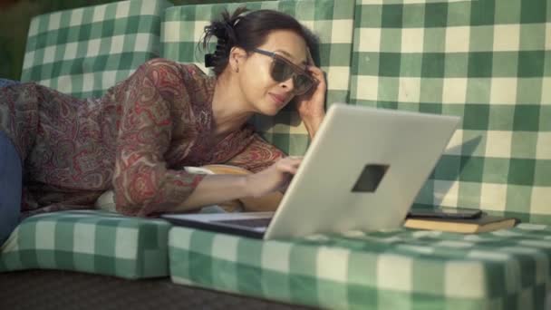 Asiatico donna in occhiali da sole con laptop rispondere al suo smartphone — Video Stock