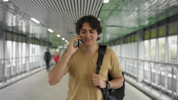Ung man med ryggsäck promenader och talar på smartphone — Stockvideo