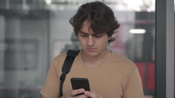 Joven frunciendo el ceño y alejándose mirando el teléfono inteligente en la estación de tren — Vídeo de stock