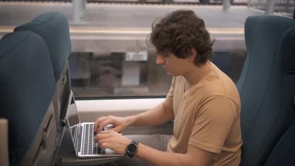 Young man in t shirt typing on laptop in the train — Stock Video