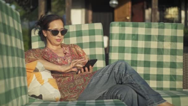 Edad media mujer asiática web surf en su teléfono inteligente en su patio — Vídeos de Stock