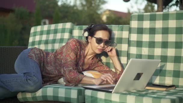 Aziatische vrouw die buiten liggen en typen op laptop — Stockvideo