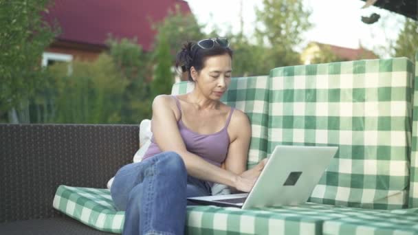 Aziatische vrouw te typen op de laptop in haar tuin — Stockvideo