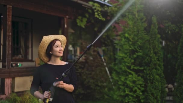 Вид збоку на азіатку в солом'яному капелюсі, що поливає дерева зі шланга — стокове відео
