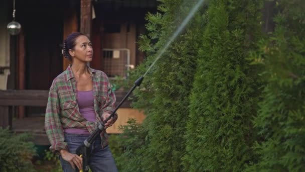 Middle aged asian woman watering trees from a hose — Stock Video