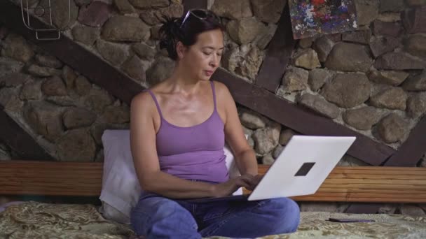 Mujer asiática escribiendo en el ordenador portátil en casa y hablando en el teléfono inteligente — Vídeo de stock
