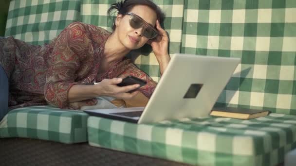 Asiatische Frau mit Sonnenbrille, die draußen ihr Telefon annimmt — Stockvideo