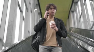 Smartphone cep telefonu ile yürüyen merdiven üzerinde konuşan genç adam