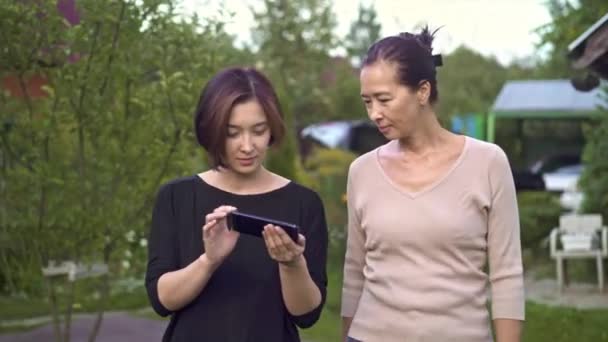 Madre e hija caminando y mirando fotos en el teléfono inteligente — Vídeos de Stock