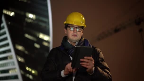 Middellange schot van architect vooruit in gele helm met een tablet — Stockvideo