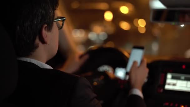 Empresário dirigindo um carro na cidade noturna rolando no telefone — Vídeo de Stock