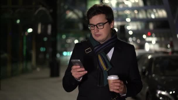 Чоловік тримає каву, що йде ввечері посміхаючись за повідомленням — стокове відео