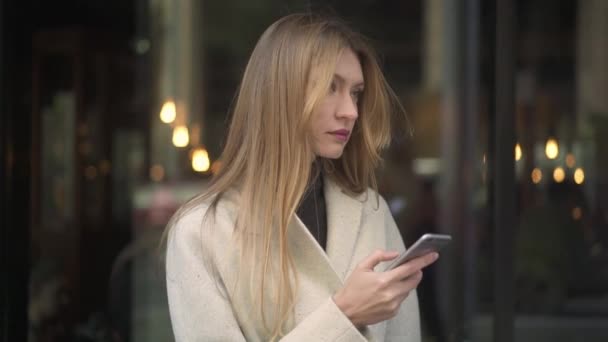 Mujer atractiva en abrigo blanco sosteniendo un teléfono mensajes de texto — Vídeos de Stock