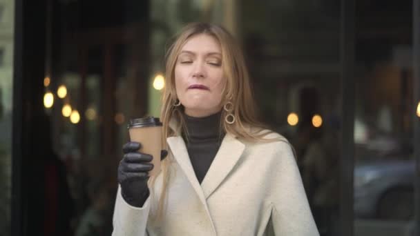 Aantrekkelijke vrouw in witte jas drinken koffie kijken naar de camera — Stockvideo