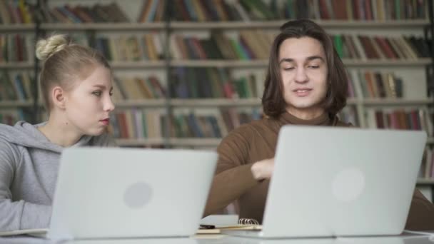 Dos jóvenes estudiantes simpáticos hembra y macho teniendo un dalogue en la biblioteca — Vídeo de stock