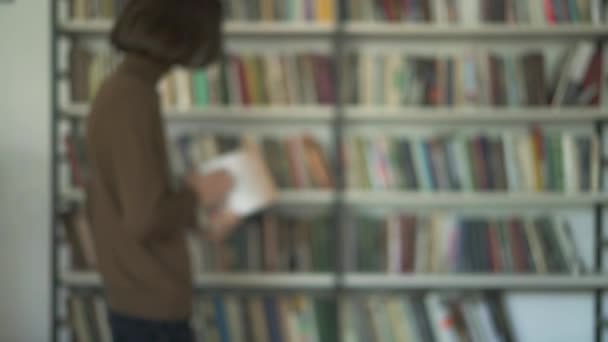 Imagen borrosa de un estudiante masculino recogiendo un libro de la estantería de la biblioteca — Vídeo de stock