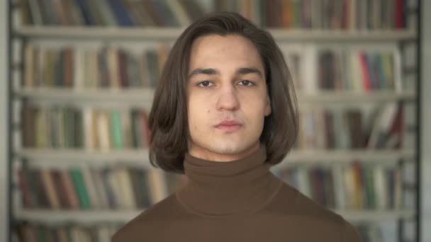 Портрет молодого красивого студента на фоне книжной полки — стоковое видео
