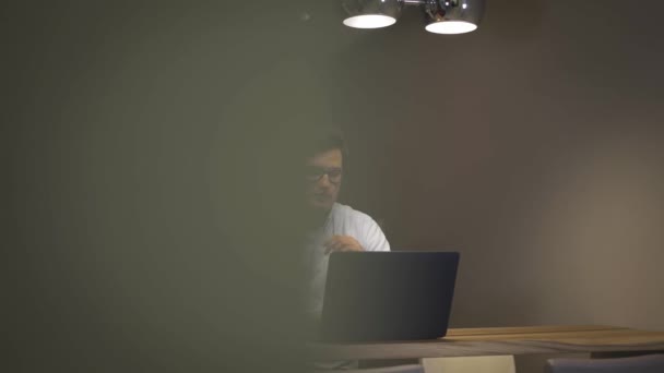 Mladý muž, pracující s přenosným počítačem, psaní si informace v poznámkovém bloku — Stock video
