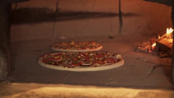 Pan shot of two vegaterians pizza into the brick oven — Stock Video