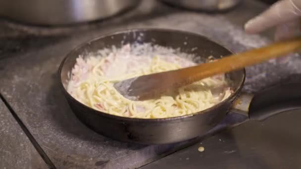 Koka holding omrörning spaghetti med ostsås och hackad bacon stekning i het panna — Stockvideo