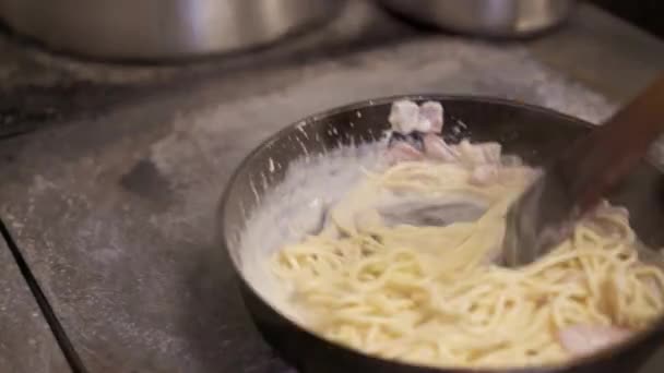 Koka holding omrörning spaghetti med ostsås och hackad bacon stekning i het panna — Stockvideo