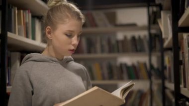 Genç sarışın kız raflardan kütüphanede arasında bir kitap duran okuma