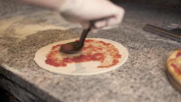 Cook přidávání rajčatový protlak na základně pizzy a ležela strouhaný sýr — Stock video