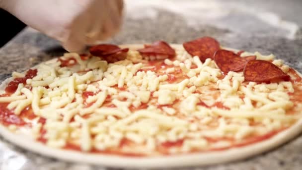 Koken handen plakjes pepperoni zetten pizza met kaas — Stockvideo