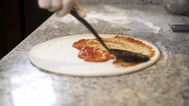 Koch fügt Tomatenmark mit einem Kochlöffel auf Pizzateig-Basis hinzu — Stockvideo