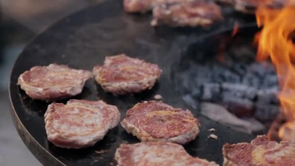 Filetes de cerdo asados en parrilla redonda de hierro fundido durante el mercado callejero — Vídeos de Stock