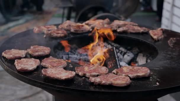 Filetes de cerdo asados en parrilla redonda de hierro fundido durante el mercado callejero — Vídeos de Stock