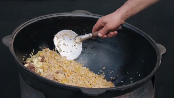 Mezclar pilaf de cocina con carne en un kazan grande en un espacio abierto — Vídeos de Stock