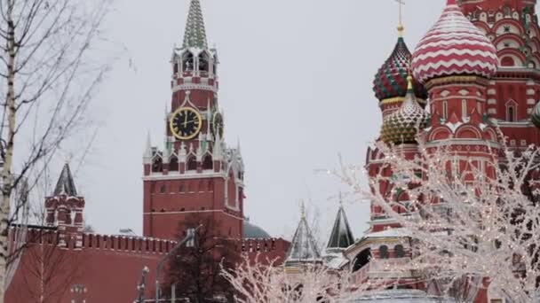 MOSCA, RUSSIA - DICEMBRE 2018: Inclinazione al rallentatore della Cattedrale di San Basilio e della Torre Spasskay nella neve di giorno con ghirlande in primo piano — Video Stock