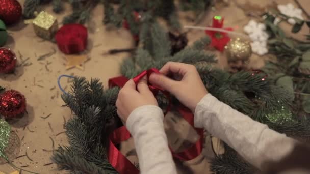 Vrouwelijke handen aanscherping van een rood lint op een kerst krans — Stockvideo