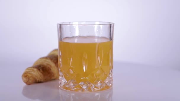 Croissant med glas saft roterande på vit bakgrund — Stockvideo