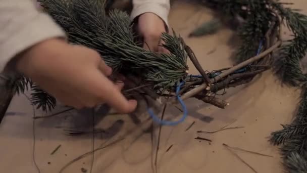 Детские руки закручивают ветви рождественской елки, делая венок — стоковое видео