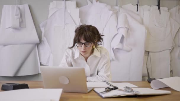 Diseñador femenino está mirando a la computadora portátil en el fondo de los patrones — Vídeo de stock